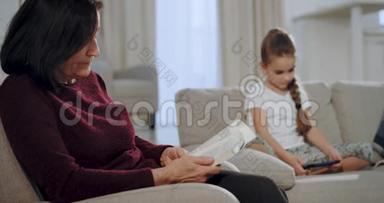 特写一位<strong>老奶奶</strong>读了一本书，看着她的侄女坐在沙发上玩智能手机的游戏